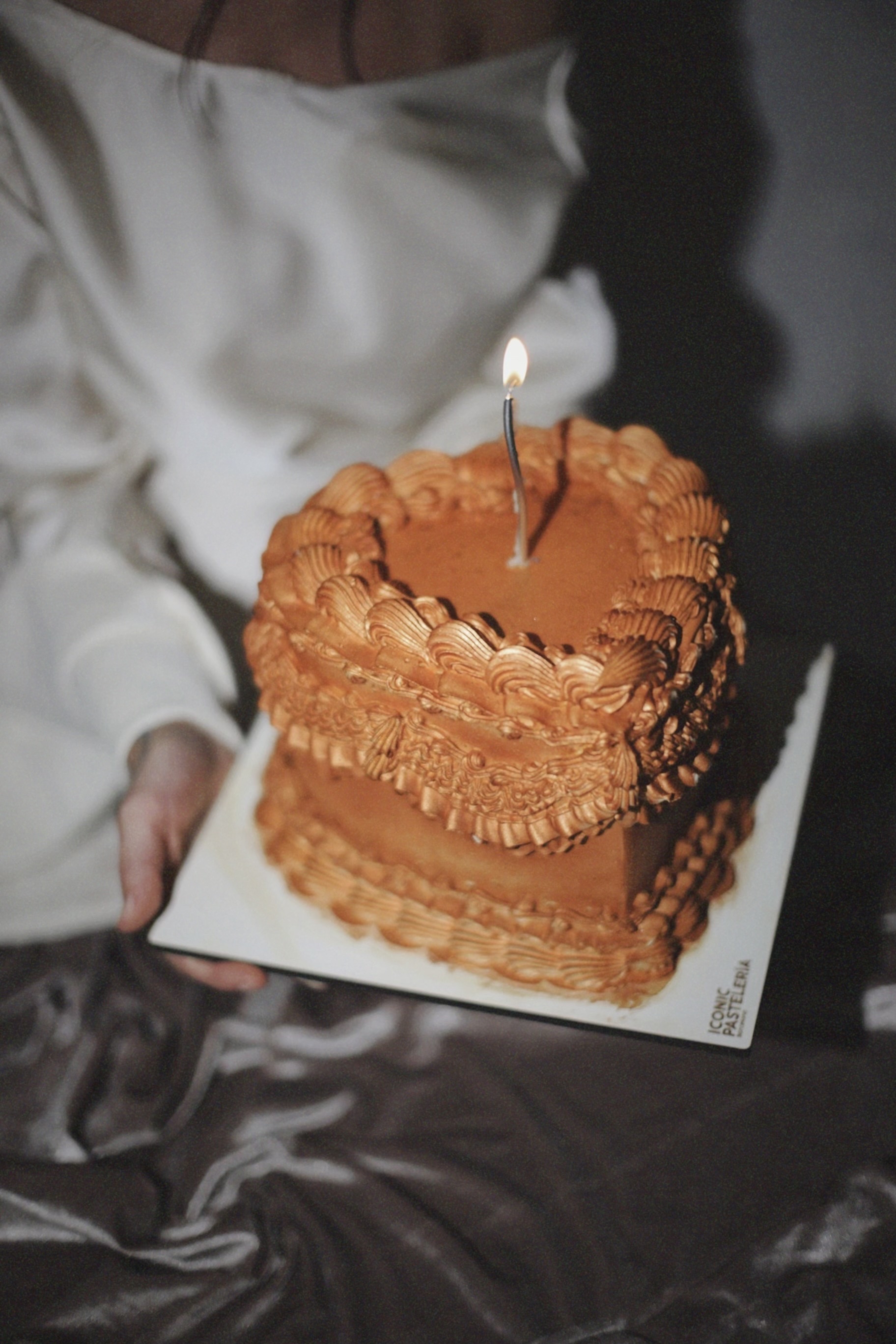 Tarta corazón vintage color caramelo con una vela encendida, sostenida sobre una base blanca